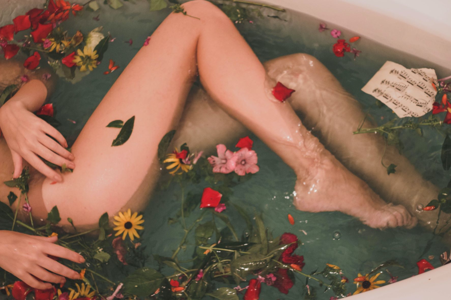image of legs in the bath with flowers floating in water
