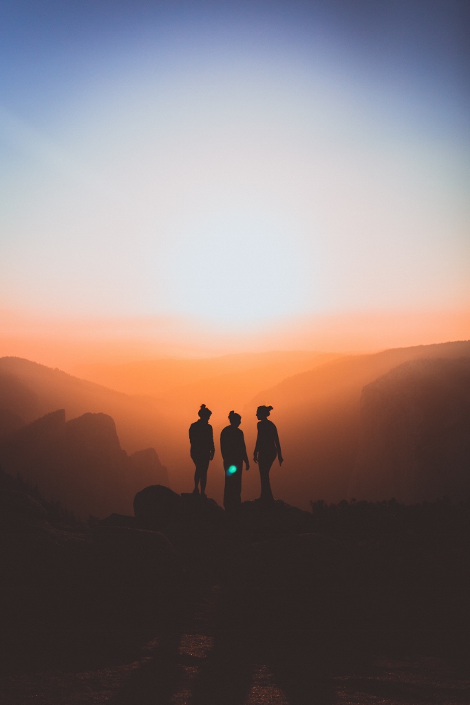 Group of people standing on mountain overlooking hazy sunrise