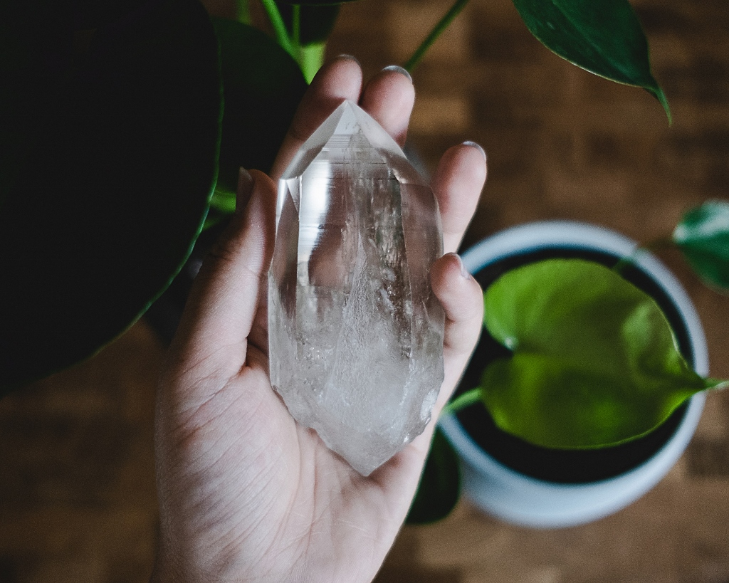 quartz crystal in a hand with plant in background